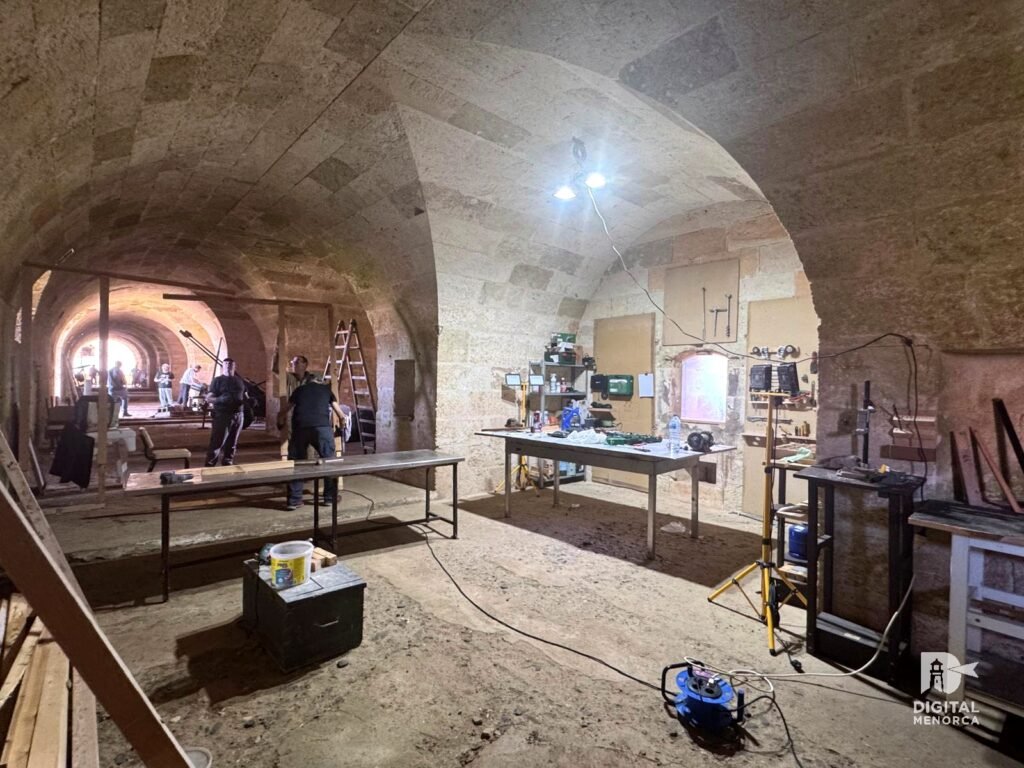 Espacio de trabajo iluminado dentro de la galería del fuerte con mesas, herramientas y restauradores preparando la intervención.